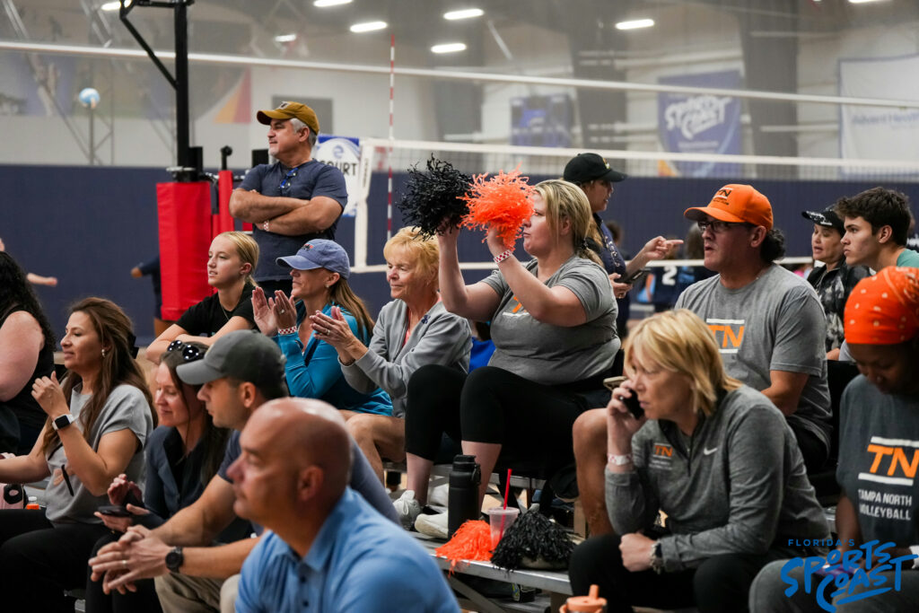 A diverse group of people sitting in a gym, enthusiastically cheering and supporting an event or activity.