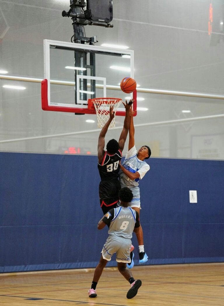 Two athletes jump simultaneously, reaching for the basketball in a competitive game setting.