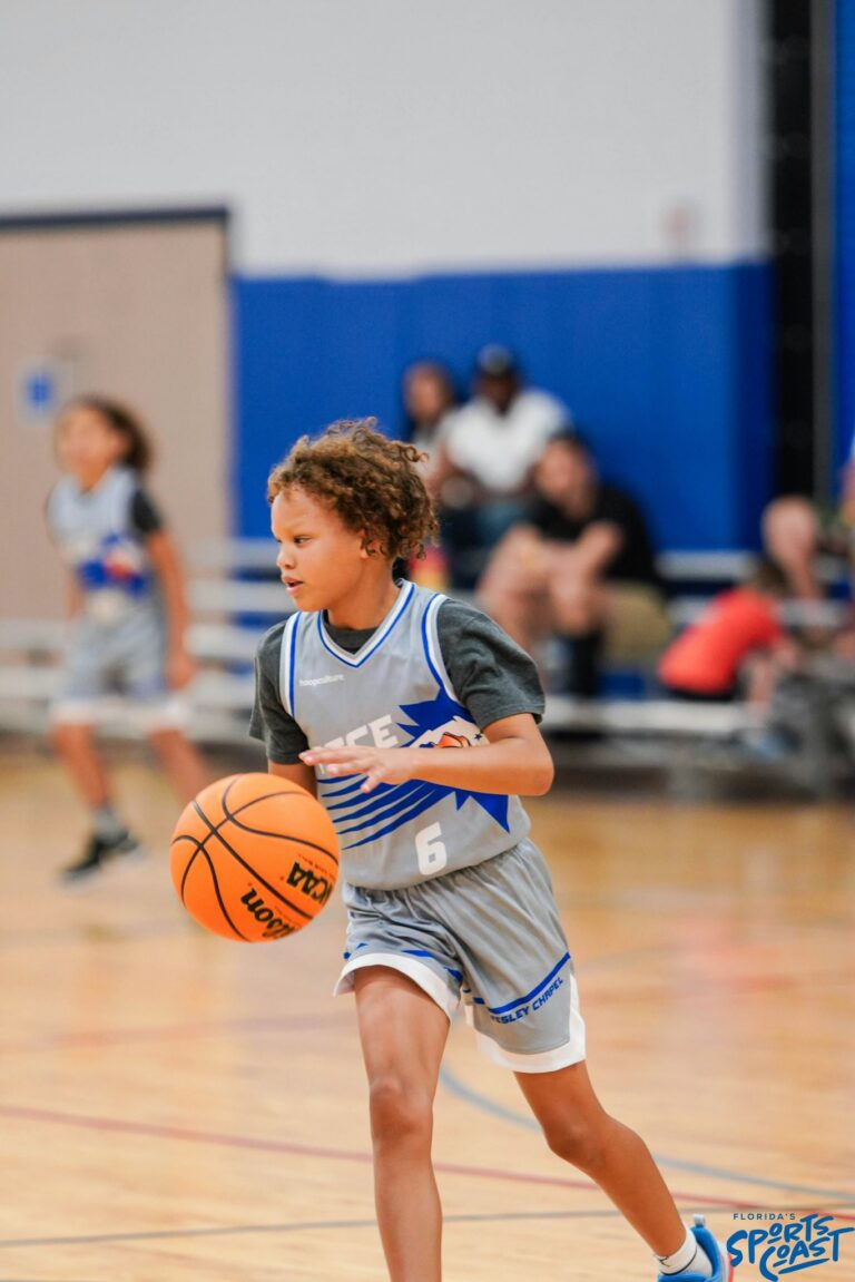 A young girl dribbles a basketball on a court, showcasing her skills and focus during practice.