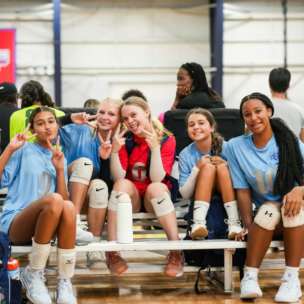 Prep and Developmental Volleyball 20 A group of young women sitting on a bench, all raising their hands in celebration or excitement.