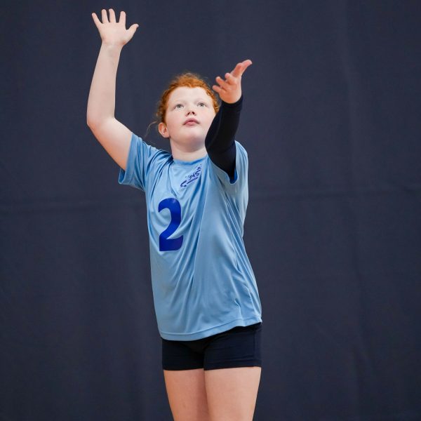 Prep and Developmental Volleyball 21 A girl in a blue shirt and black shorts strikes a volleyball during a game on a sandy court