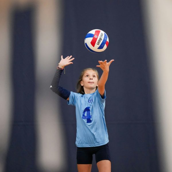 Prep and Developmental Volleyball 22 A girl in a blue shirt and black shorts strikes a volleyball during a game on a sandy court