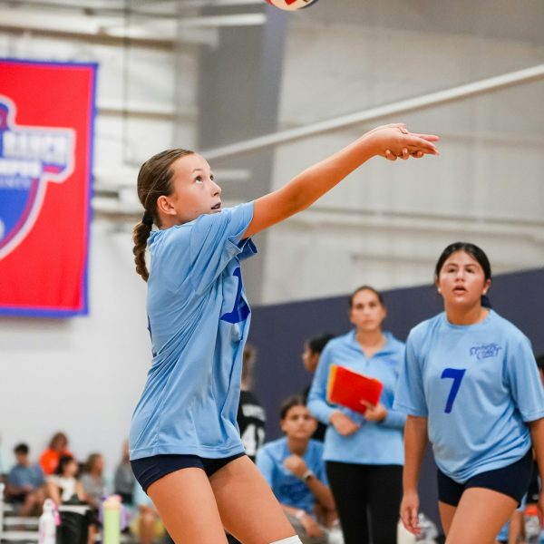 Prep and Developmental Volleyball 23 A girl in a blue shirt and black shorts strikes a volleyball during a game on a sandy court