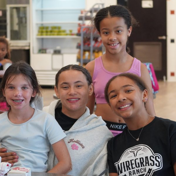 Four girls smile and pose together at a table, showcasing a joyful moment in a social setting.