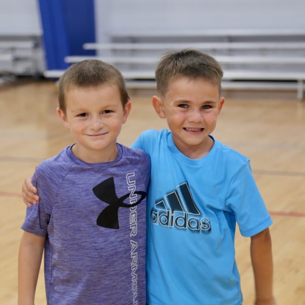 Two boys smile and pose together on a basketball court, showcasing their friendship and enthusiasm for the sport.