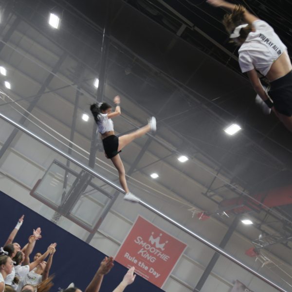 Cheerleader executing a stunt in a gym, showcasing athleticism and teamwork with teammates supporting her.