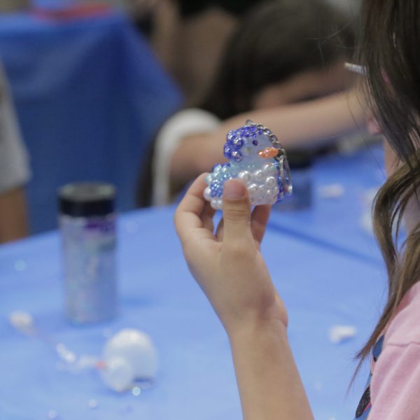 A girl sits at a table, holding a small plastic bird in her hand, smiling at the camera.