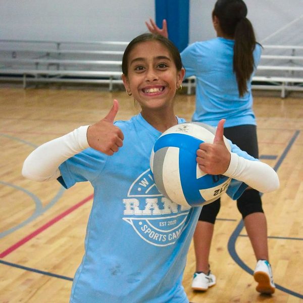 A girl in a blue shirt and black shorts strikes a volleyball during a game on a sandy court