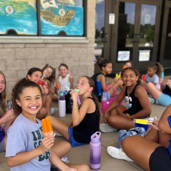 A group of girls sitting on the ground, enjoying ice cream cones on a sunny day.