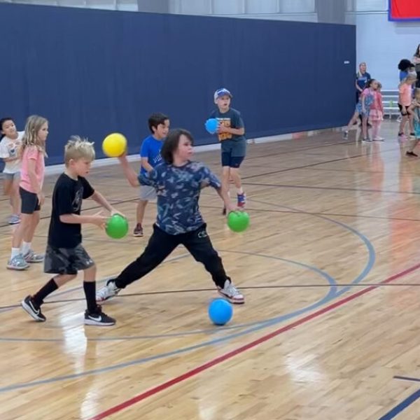 A group of children joyfully playing with colorful balls in a spacious gymnasium.