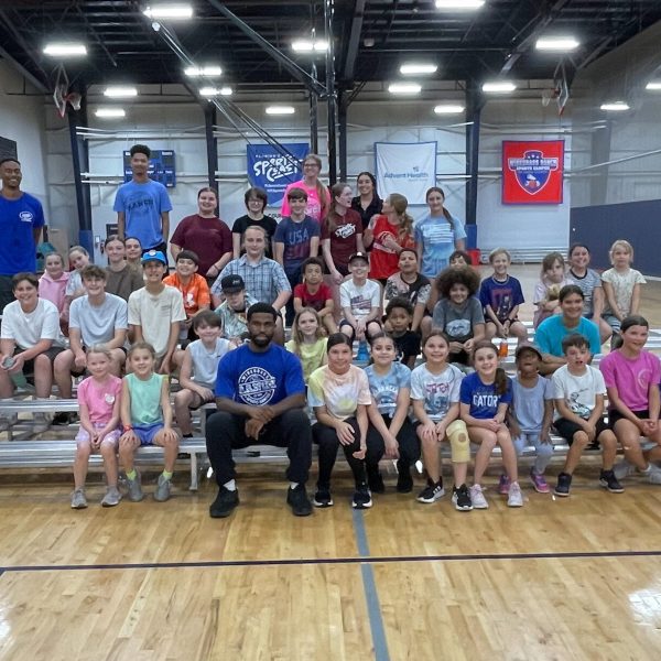A group of children and adults smiling together for a photo in a gym setting, showcasing a sense of community and joy.