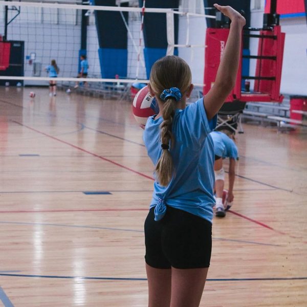 Prep and Developmental Volleyball 18 A girl in a blue shirt and black shorts strikes a volleyball during a game on a sandy court