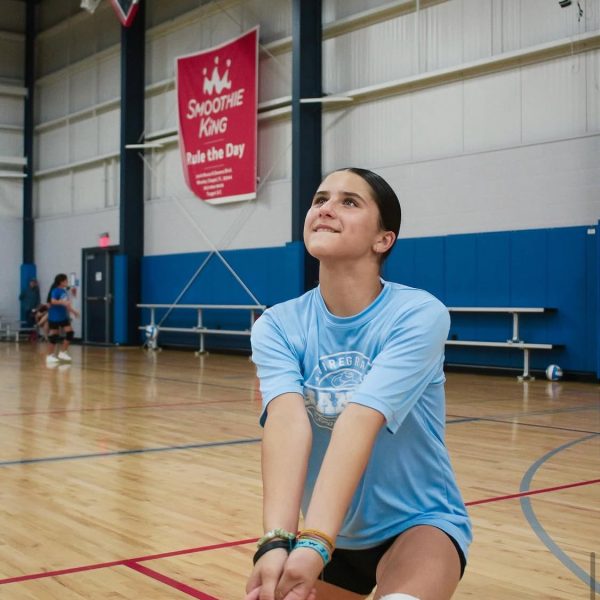 Prep and Developmental Volleyball 26 A girl in a blue shirt and black shorts strikes a volleyball during a game on a sandy court