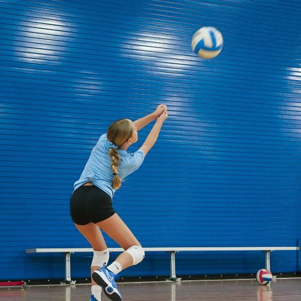 Prep and Developmental Volleyball 13 A girl in a blue shirt and black shorts strikes a volleyball during a game on a sandy court